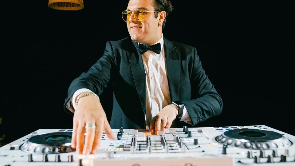 DJ Justin in a tuxedo mixing on a white DJ controller at a night event