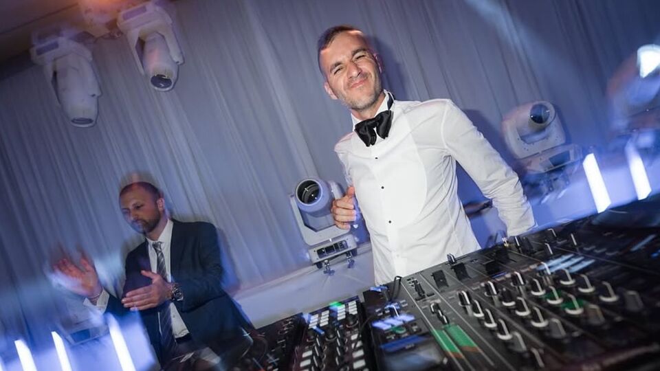 DJ Oren in a white dinner jacket at the mixer under blue moving-head lights