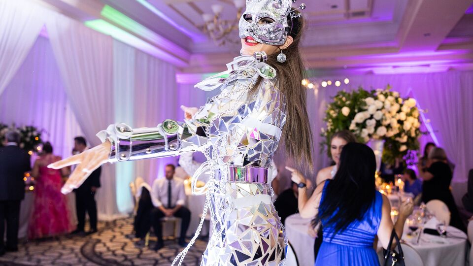 Performer in a mirrored costume and mask dancing among guests in a ballroom