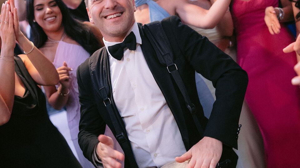 Percussionist with a strapped-on drum playing among dancing guests