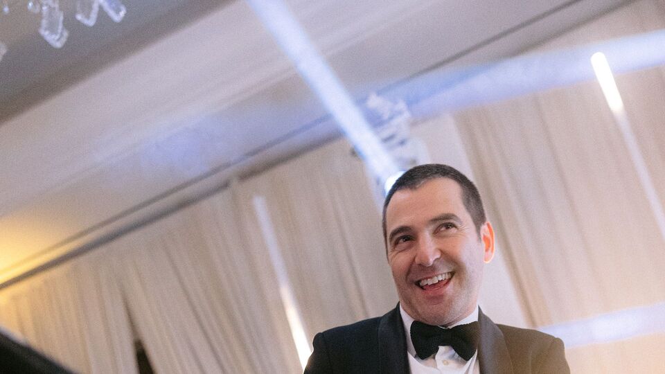 Drummer in a tuxedo smiling under white stage lights