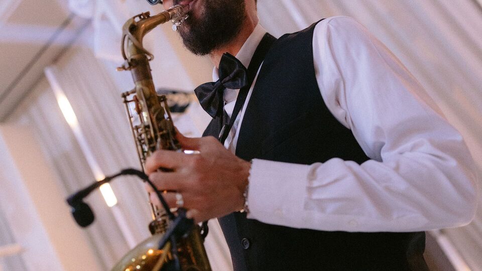 Saxophonist in a vest and bow tie playing in front of white drapes