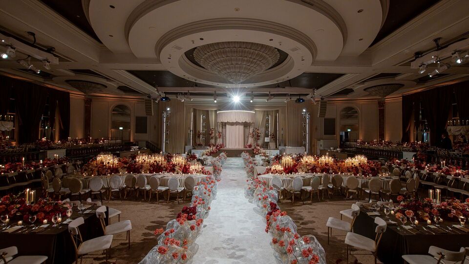 Hotel ballroom set for a wedding, a white aisle lined with red flowers between the round tables