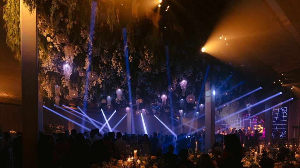 Blue light beams over the guests in a dark ballroom with a floral ceiling
