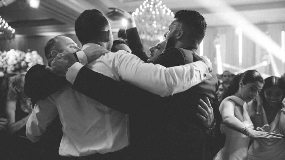 Men dancing arm in arm in a circle on a ballroom dance floor, in black and white