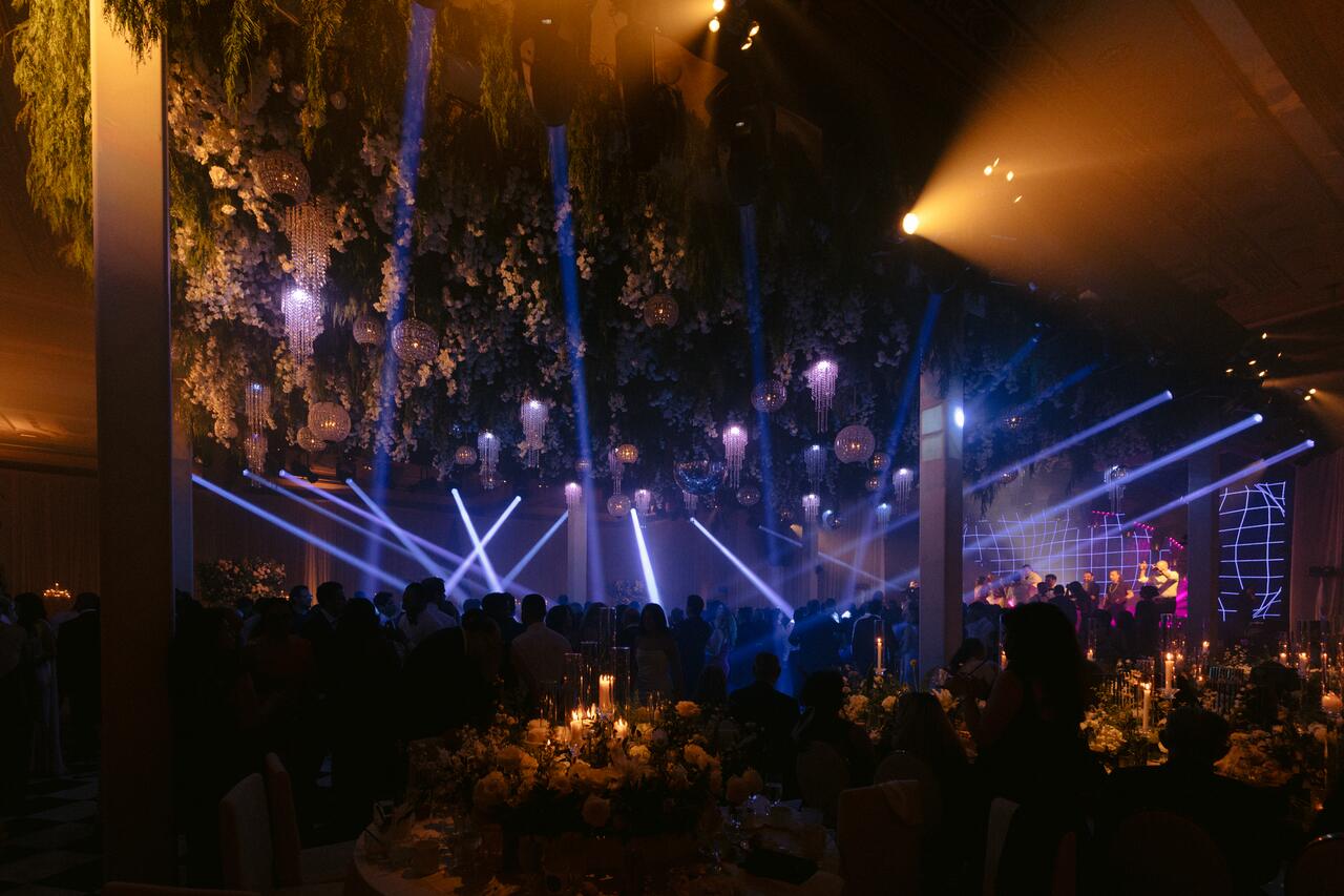 Blue beams sweeping across a tented reception under a floral ceiling