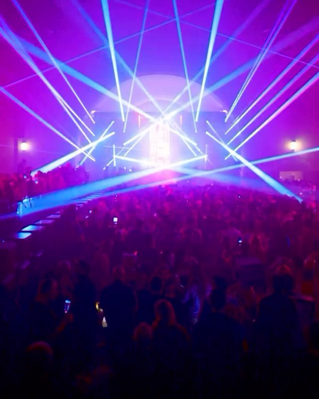 Blue and violet laser beams fanning over a packed concert crowd