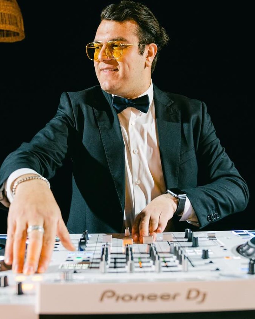 DJ Justin in a tuxedo and tinted glasses at the decks