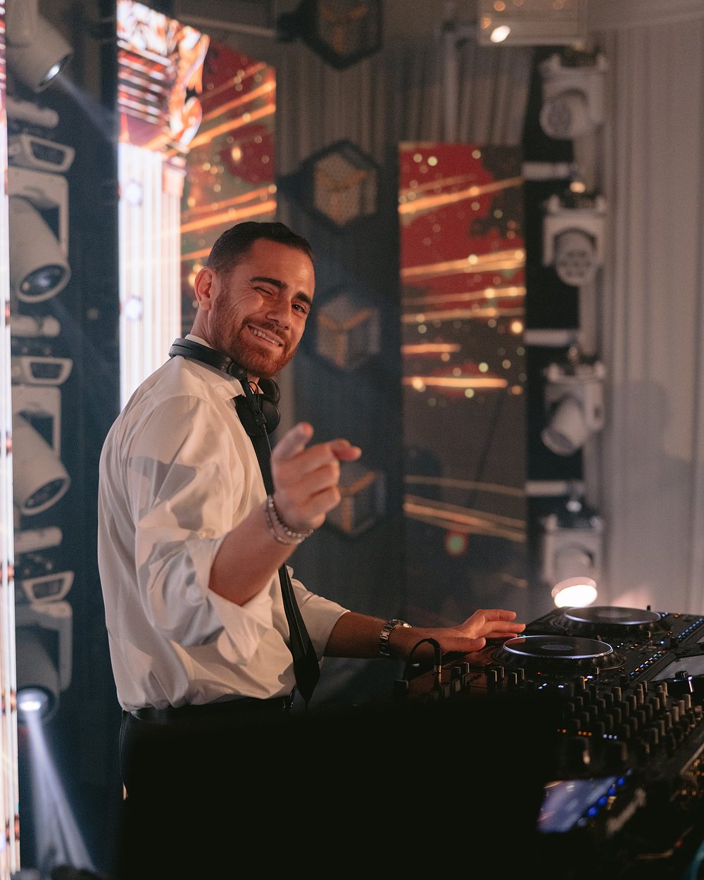 DJ Nathan smiling and pointing to camera from behind the decks
