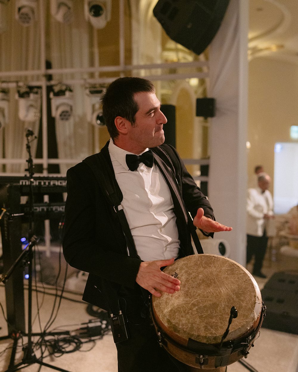 A percussionist in black tie playing a standing hand drum at a reception