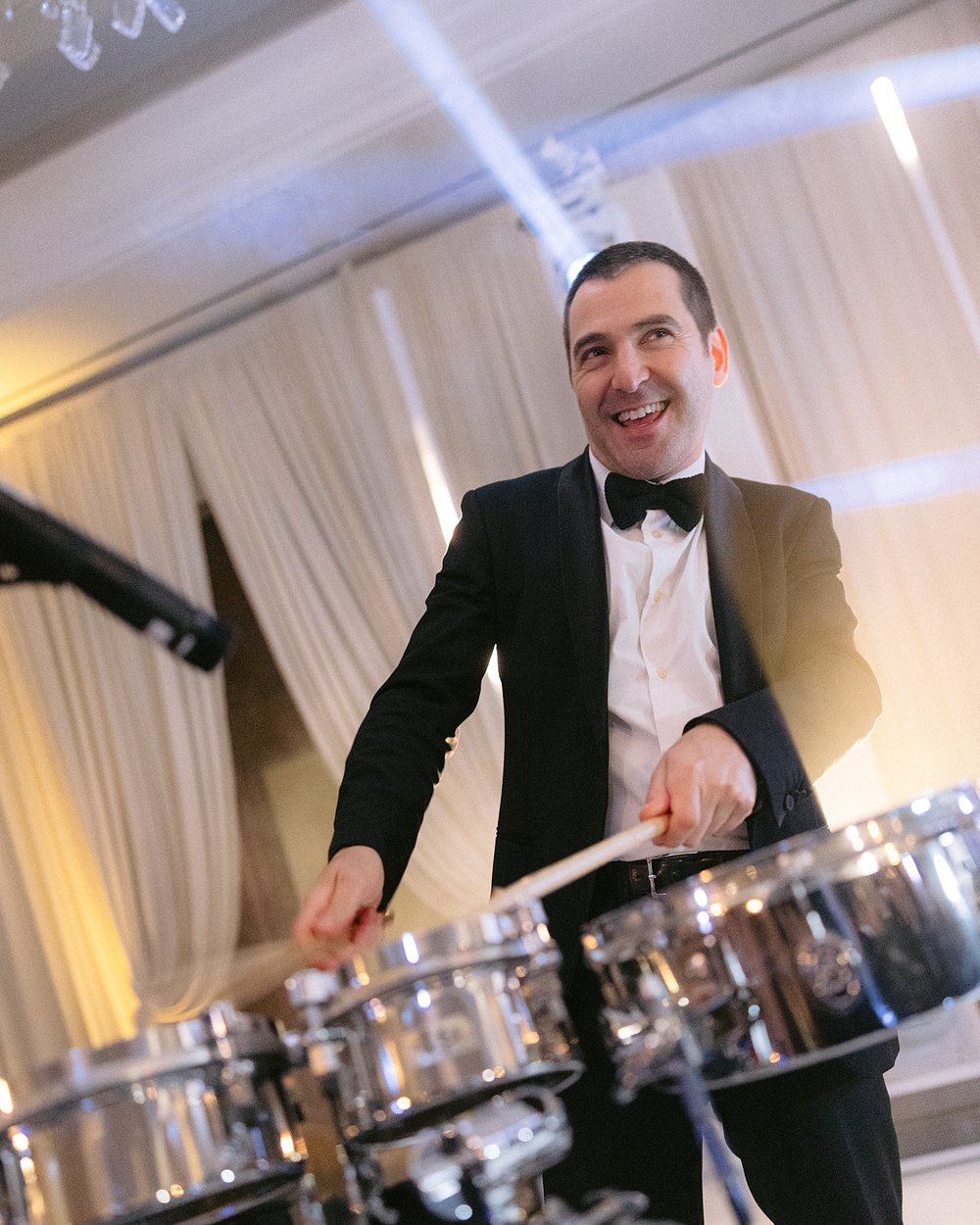 A drummer in black tie playing a timbale kit at a ballroom reception