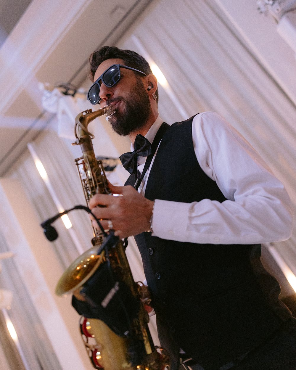 A saxophonist in a waistcoat playing an alto saxophone at a reception