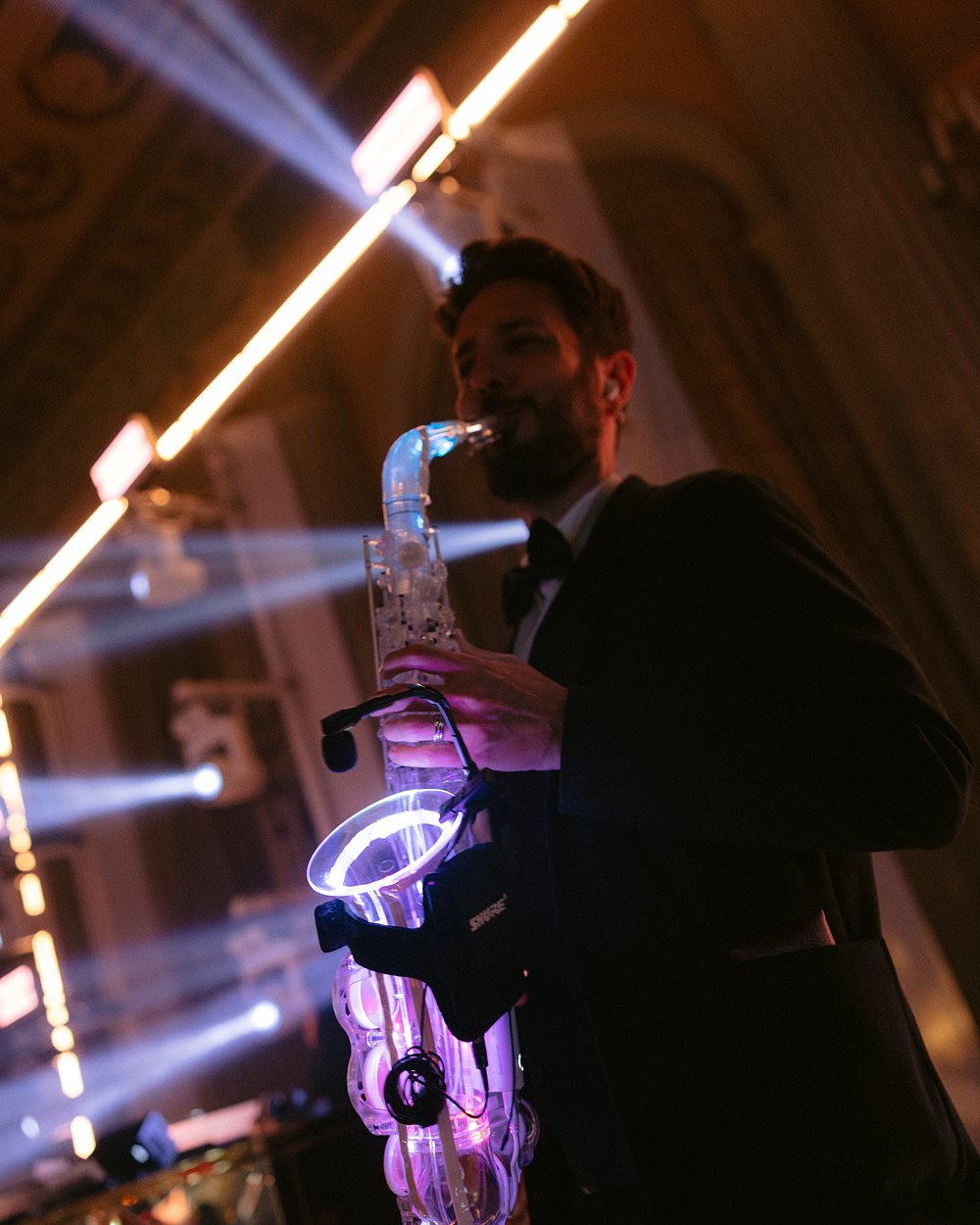 Saxophonist playing an LED-lit saxophone under beams of stage light