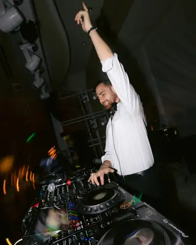 A DJ working a Pioneer controller with one arm raised in a dark room.