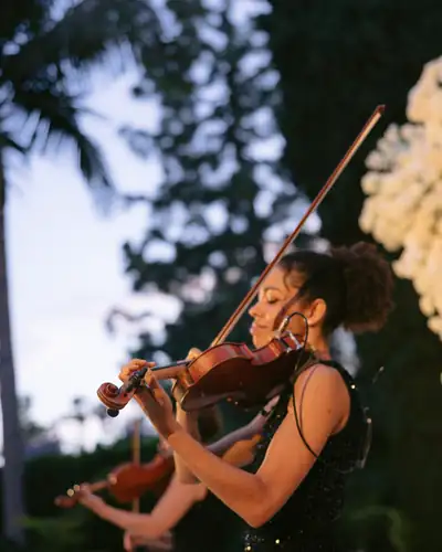 A violinist playing outdoors at a ceremony, palms behind her at dusk.