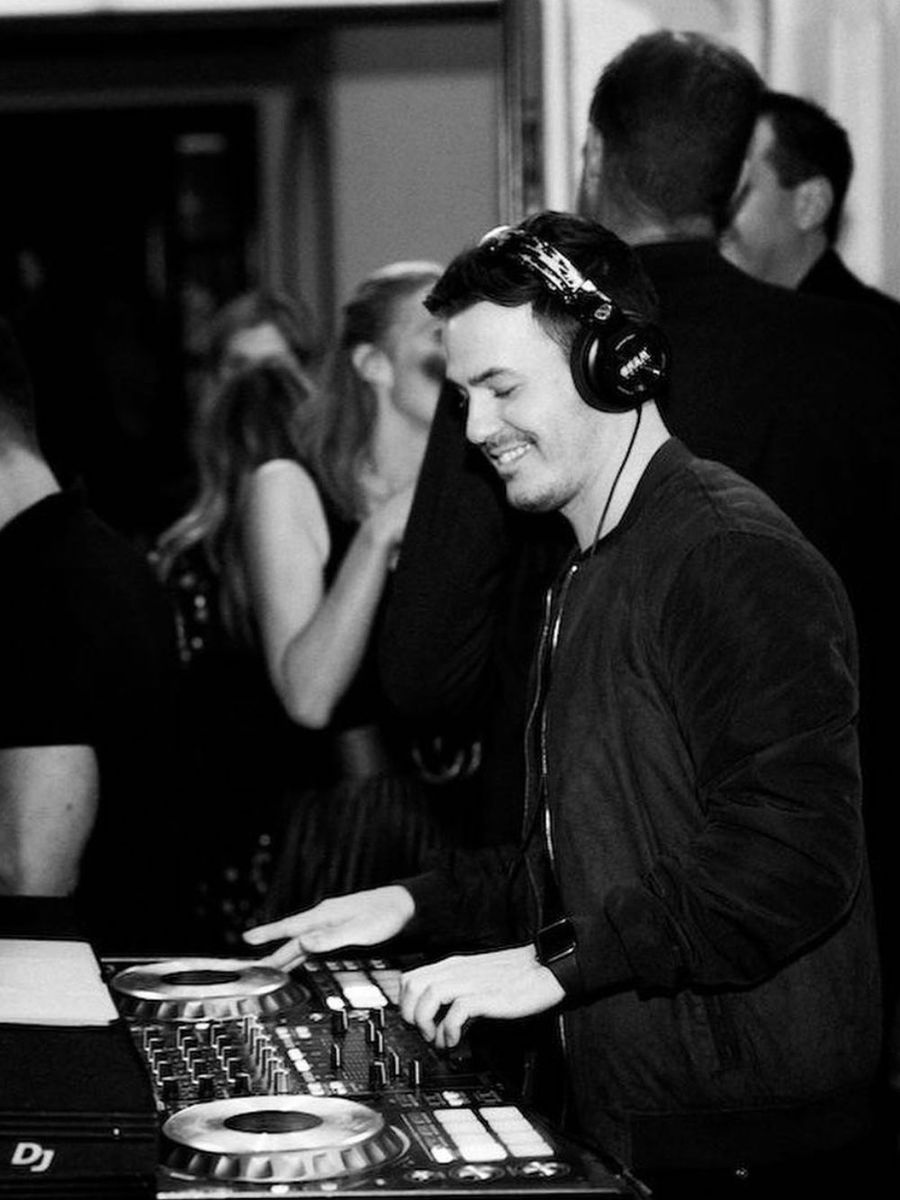 DJ Corey in headphones at a Pioneer controller with guests behind him