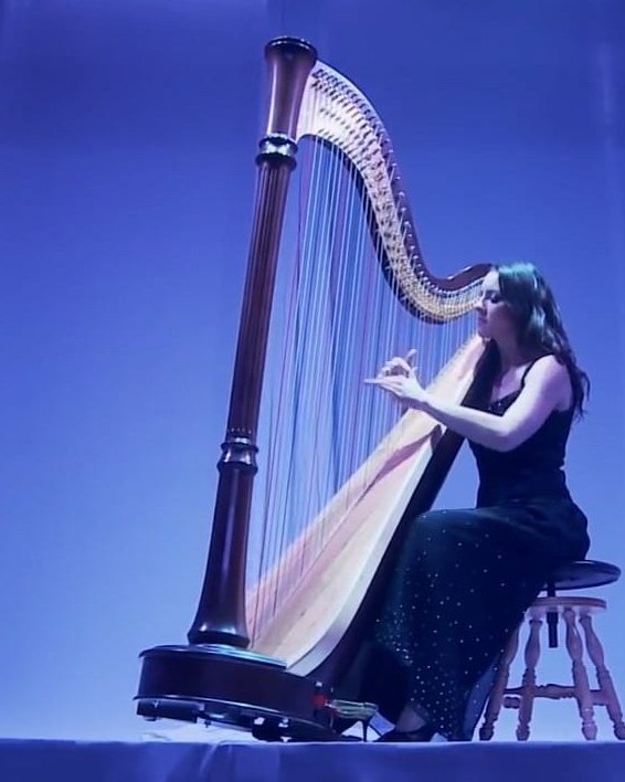 A harpist in a black gown playing a concert harp on a stage lit blue