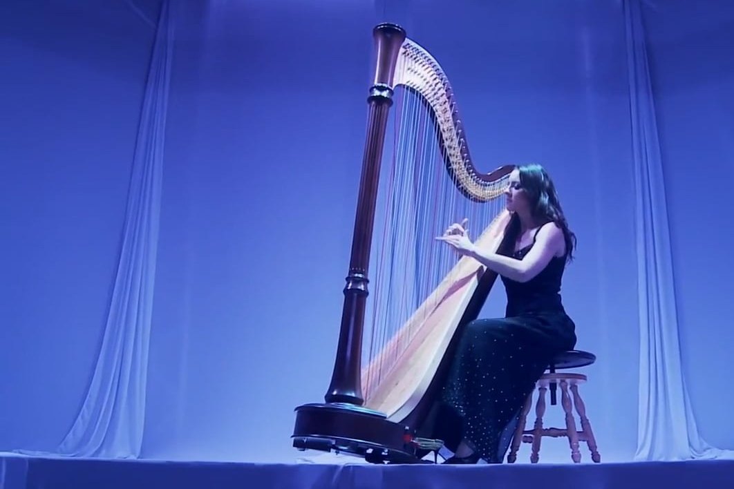 A harpist performing in front of a lit blue drape
