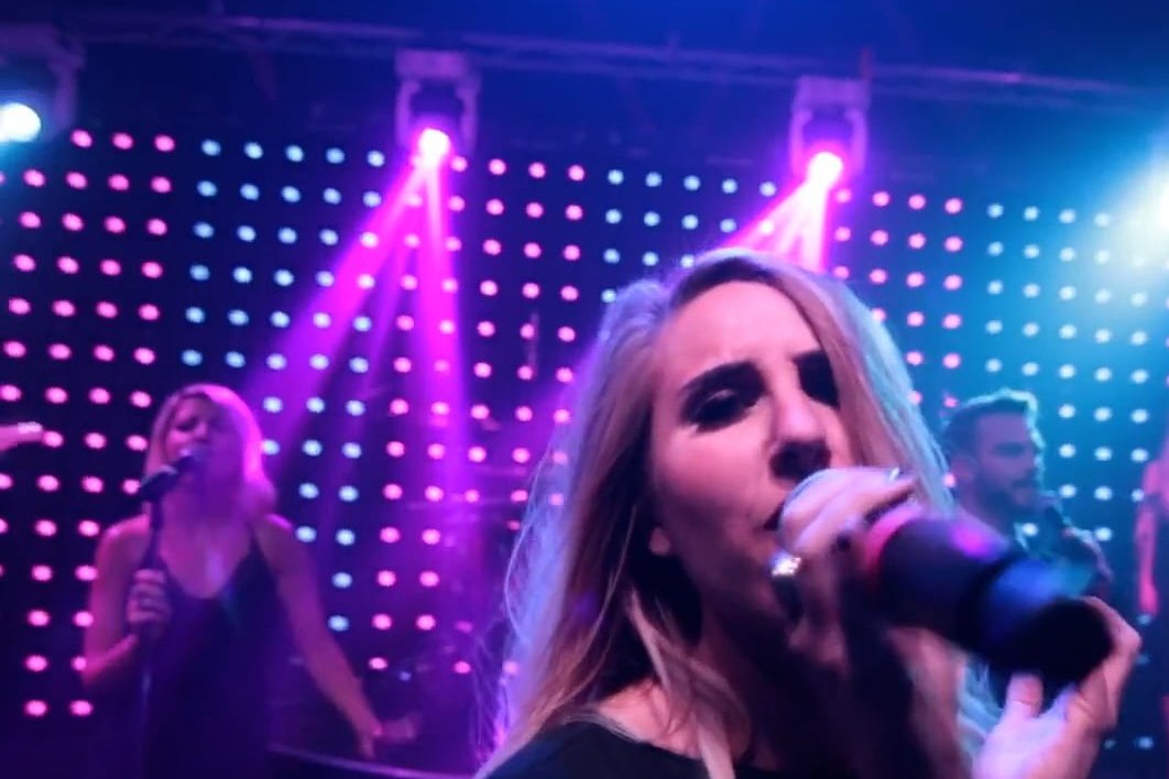 A LIV vocalist singing into a handheld microphone under stage lighting