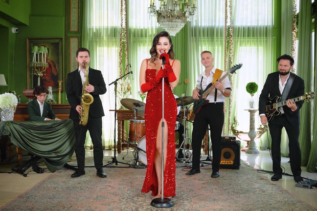 LIV Vintage's singer in a red sequinned gown at the mic, with sax, keys, drums and two guitars in a green-curtained room