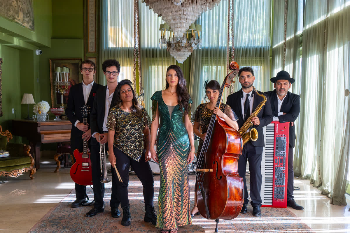Rubato's eight-piece line-up in a chandeliered room: a singer in a green sequinned gown, upright bass, sax, red guitar and red keyboard