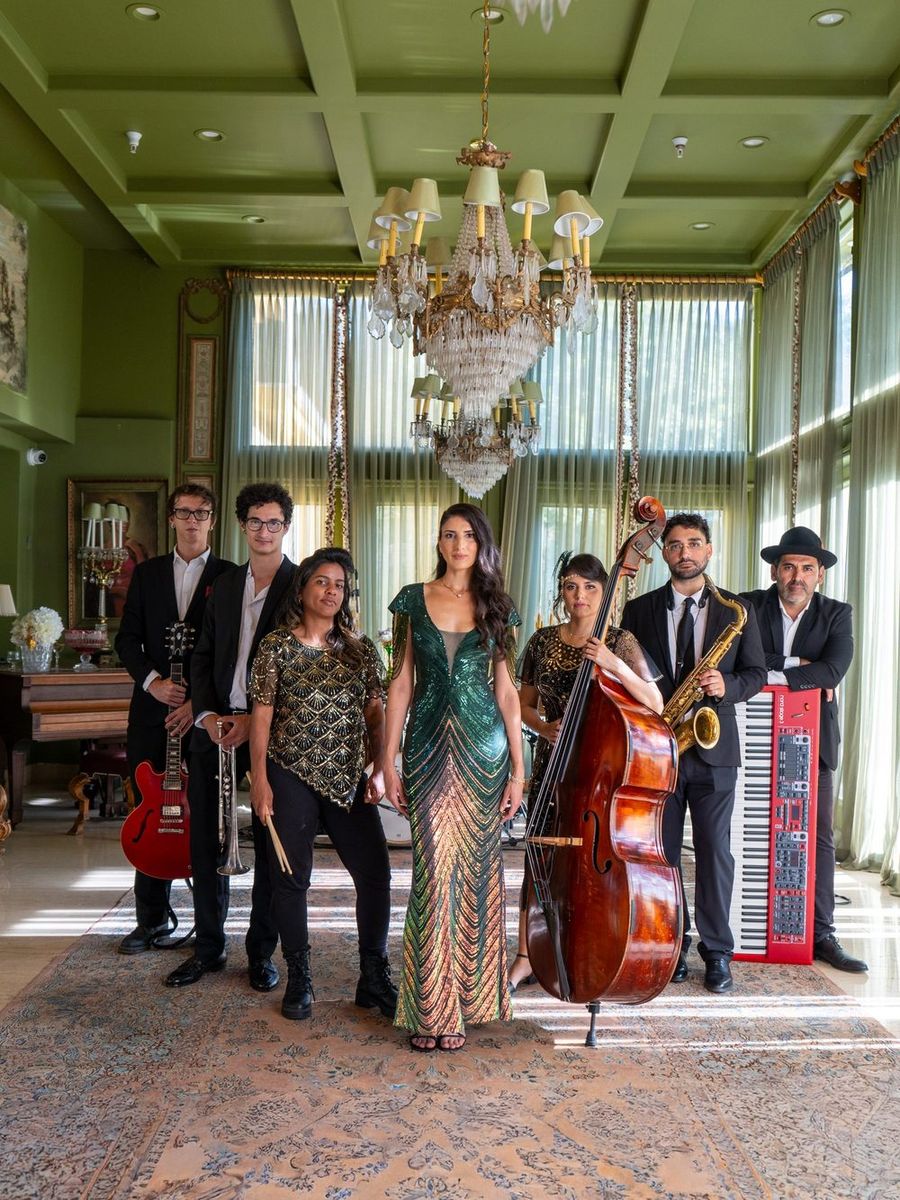 Rubato's eight-piece line-up in a chandeliered room: a singer in a green sequinned gown, upright bass, sax, red guitar and red keyboard