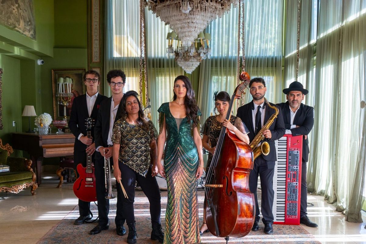 Rubato's eight-piece line-up in a chandeliered room: a singer in a green sequinned gown, upright bass, sax, red guitar and red keyboard