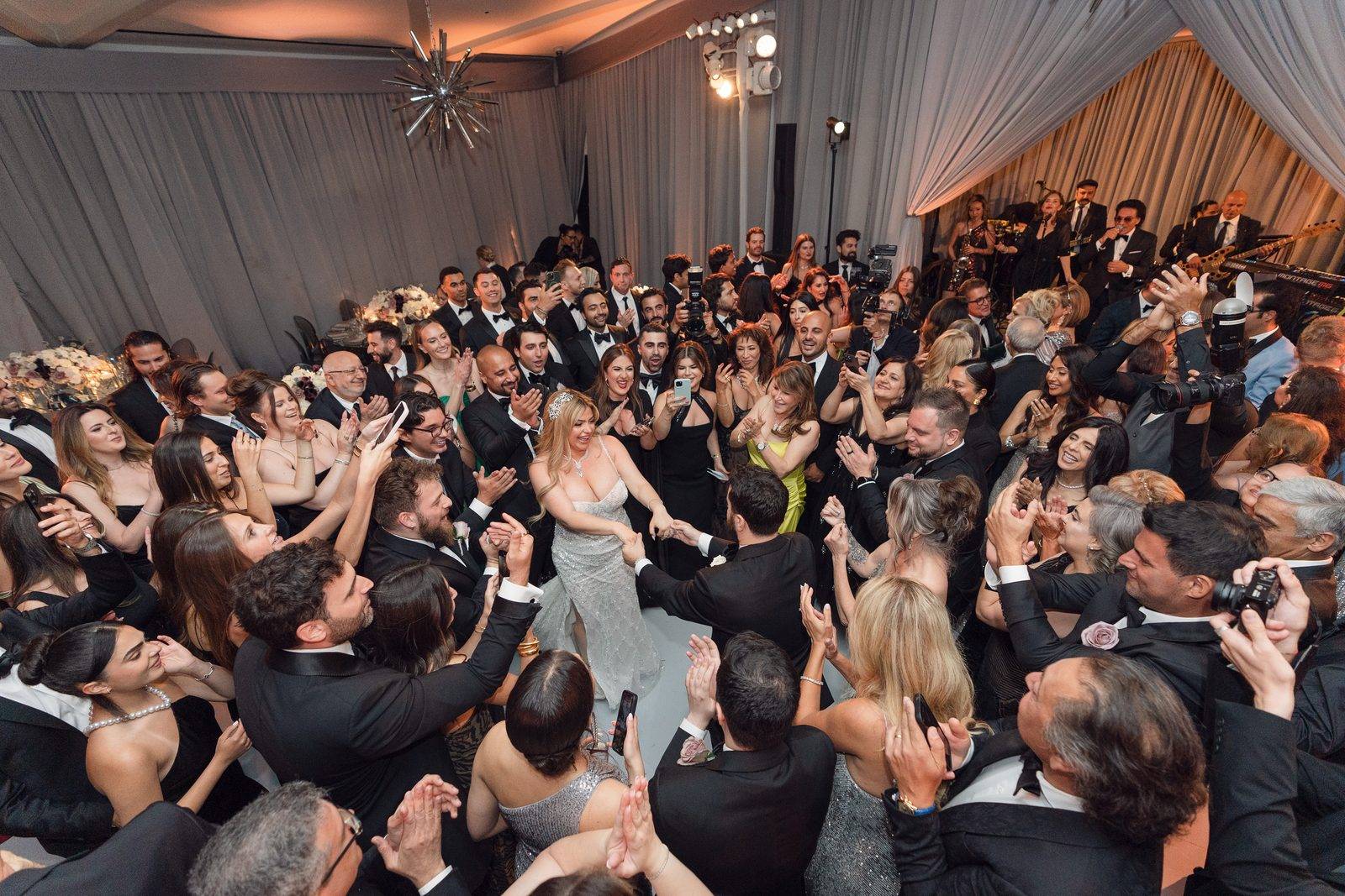 Guests circling the bride on the dance floor at Hotel Bel-Air while a live band plays from the stage behind them