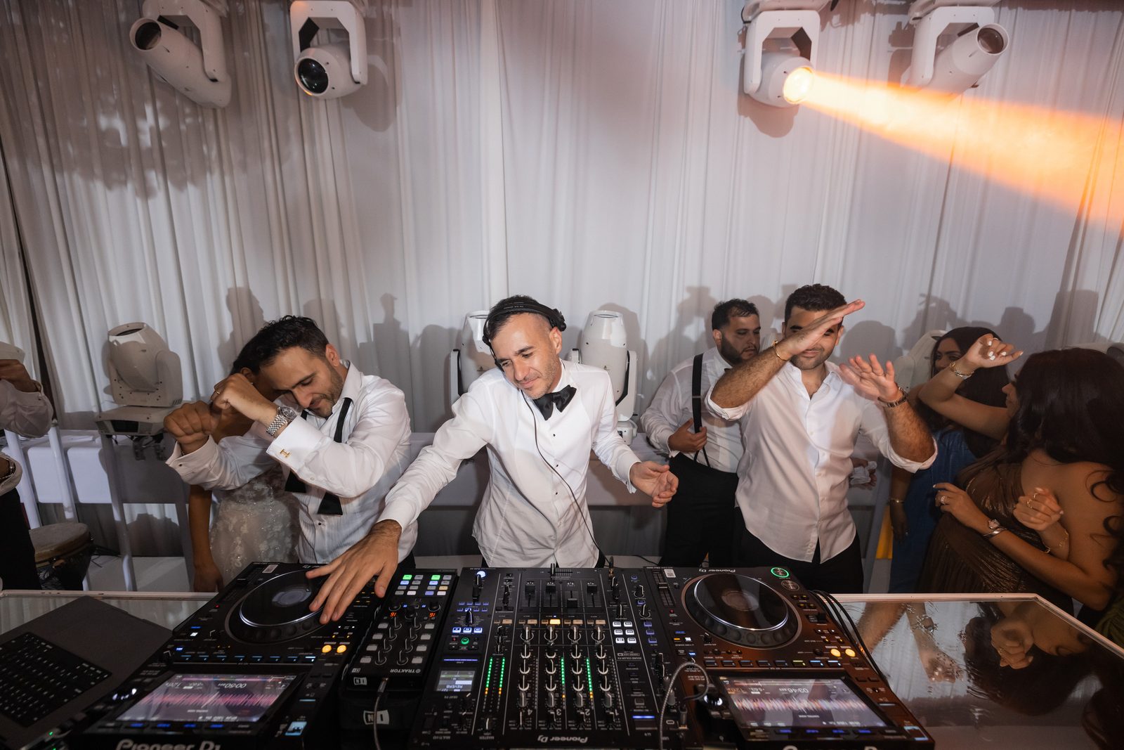 DJ working a Pioneer setup at the Four Seasons Westlake Village with an orange beam crossing the drape behind him