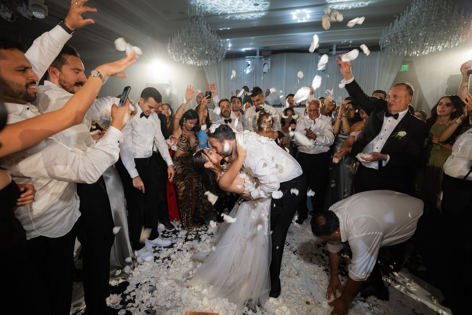 White petals falling over a couple kissing on the dance floor surrounded by cheering guests at the Four Seasons Westlake Village