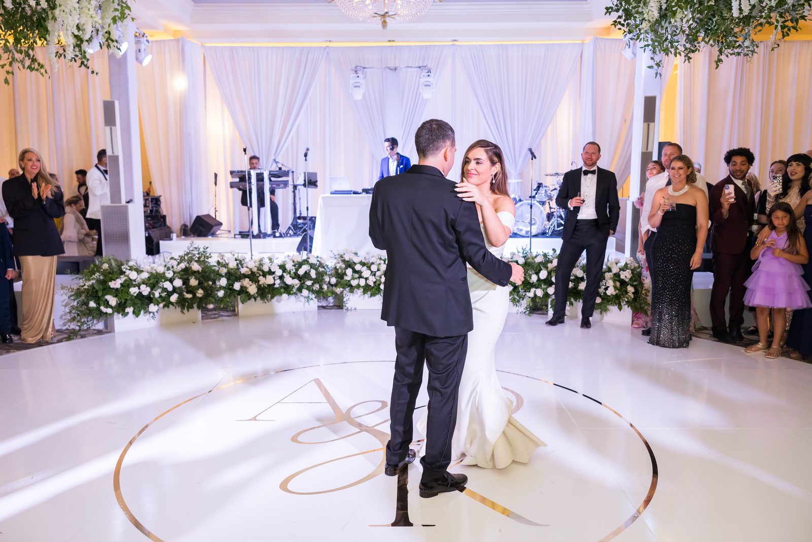 Couple holding their first dance on a white floor printed with a gold monogram at Waldorf Astoria Monarch Beach