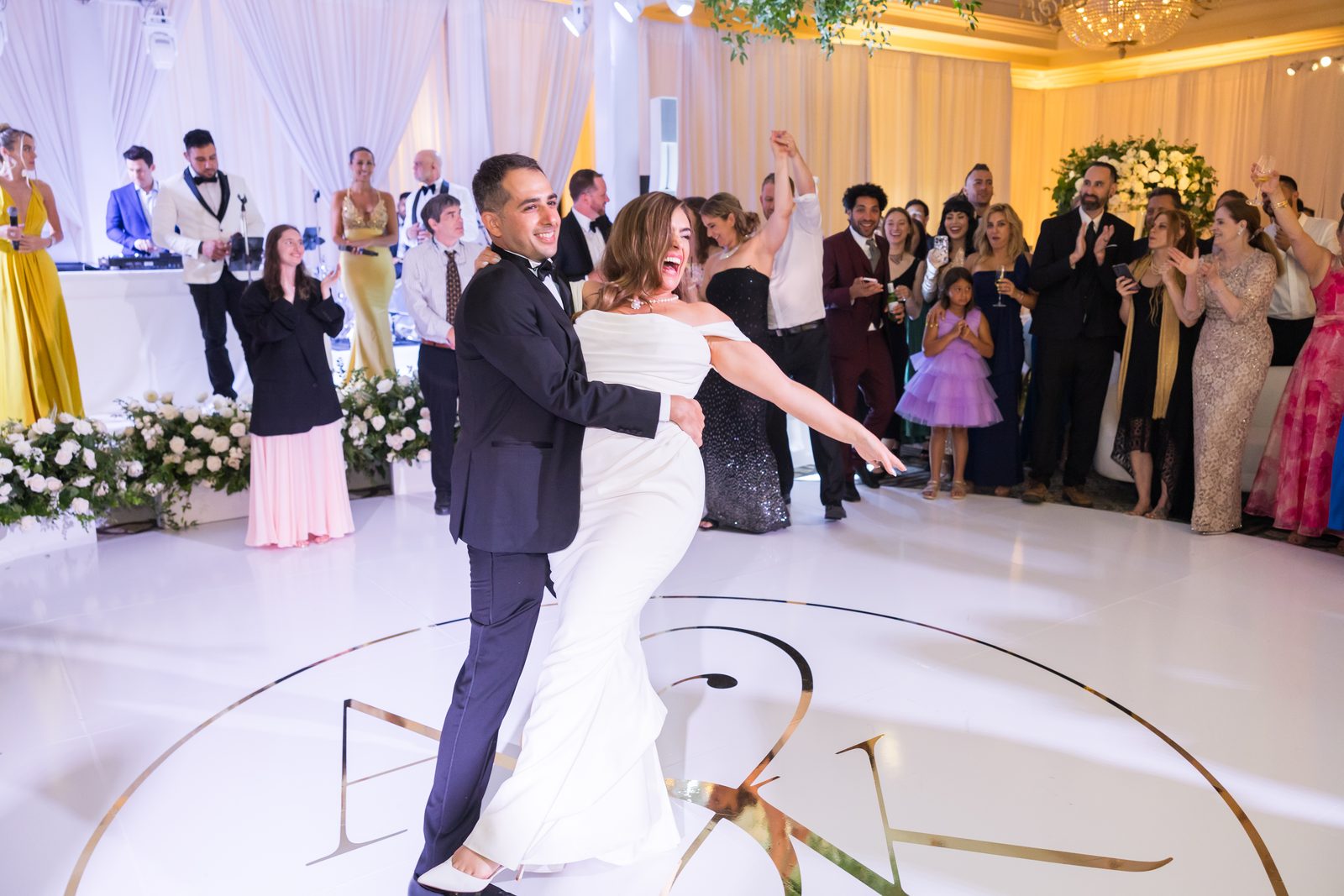 Couple stepping out laughing onto the monogrammed dance floor at Waldorf Astoria Monarch Beach as guests applaud