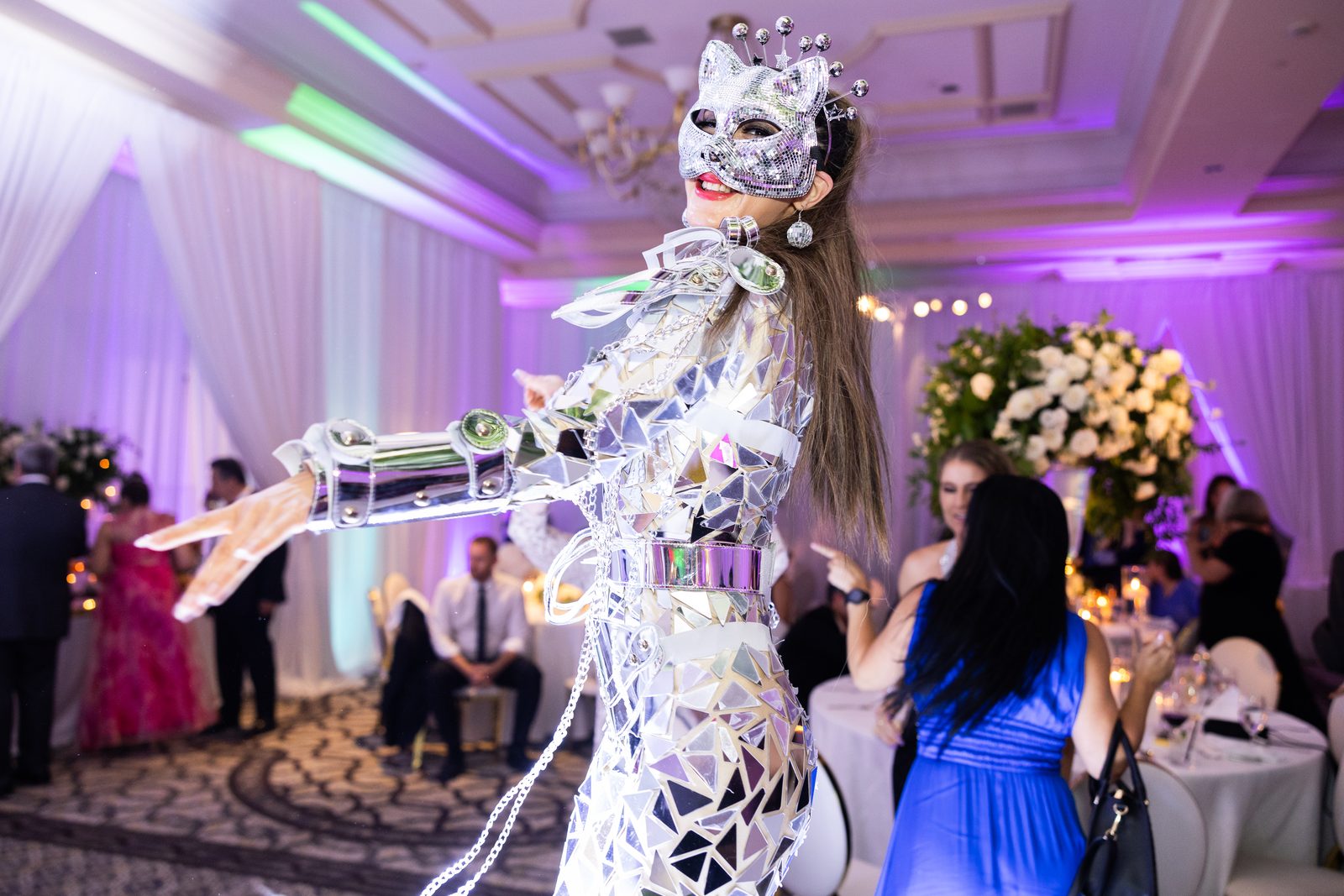 Performer in a mirrored costume moving between dinner tables at Waldorf Astoria Monarch Beach with the walls lit purple