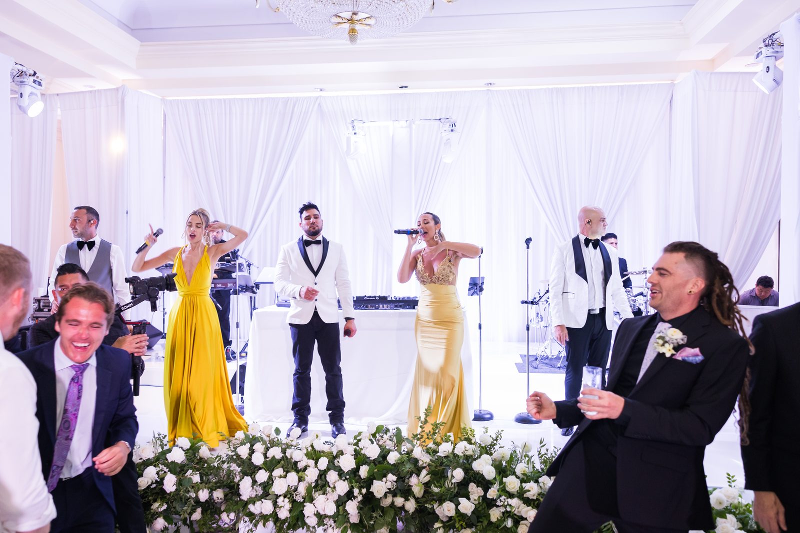 Two vocalists in gold and yellow gowns singing with the band at Waldorf Astoria Monarch Beach while guests dance in front